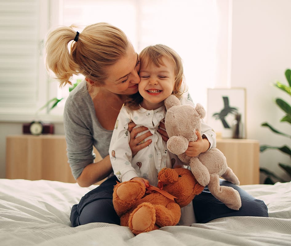 woman hugging child with teddy bear